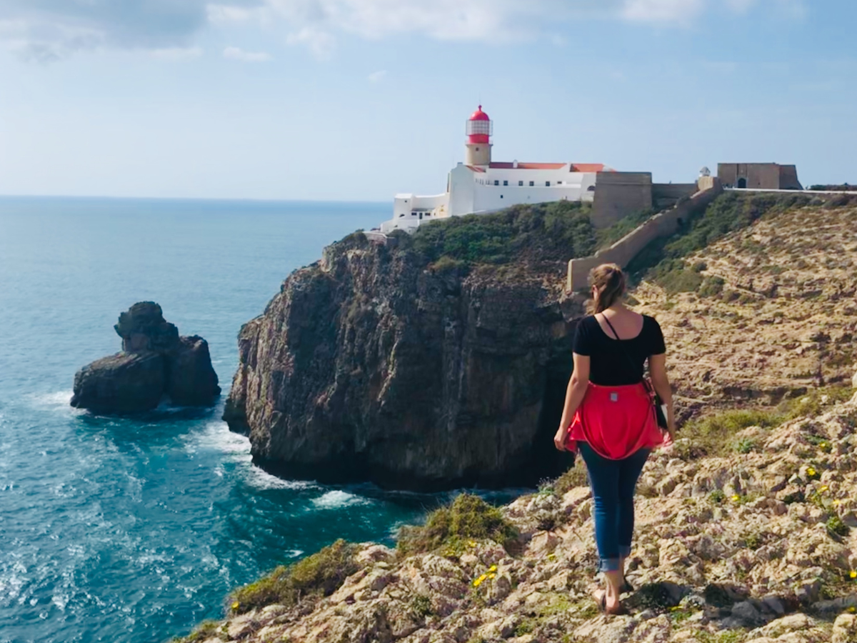 Kathi Adventures Kathi walking on a coastline with a lighthouse in the distance